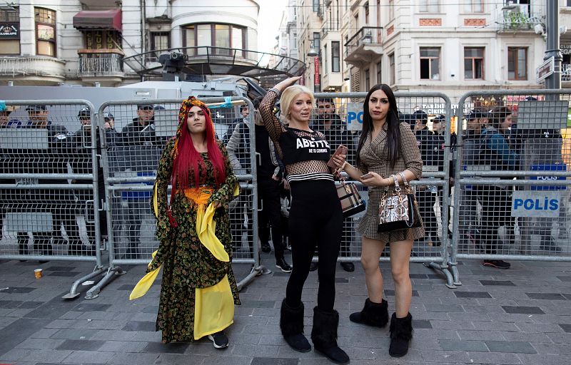 Tres mujeres tránsgenero intentan cruzar a la calle adyacente mientras la policía turca impide el paso para evitar la marcha con motivo del Día Internacional de la Mujer, este viernes en Estambul (Turquía).