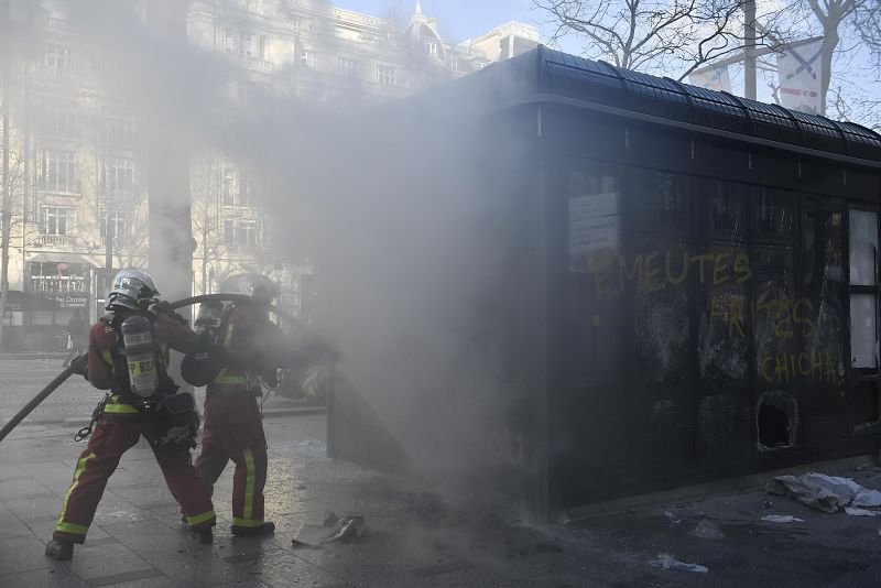 Los bomberos trabajan en las tareas de extinción de un incendio provocado en un quiosco de prensa en los Campos Elíseos