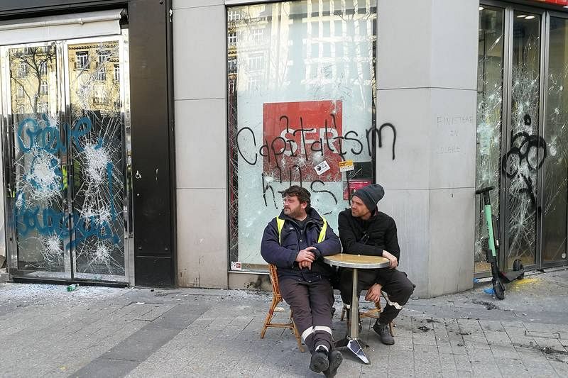 Dos manifestantes sentados frente a un escaparate dañado en los Campos Elíseos