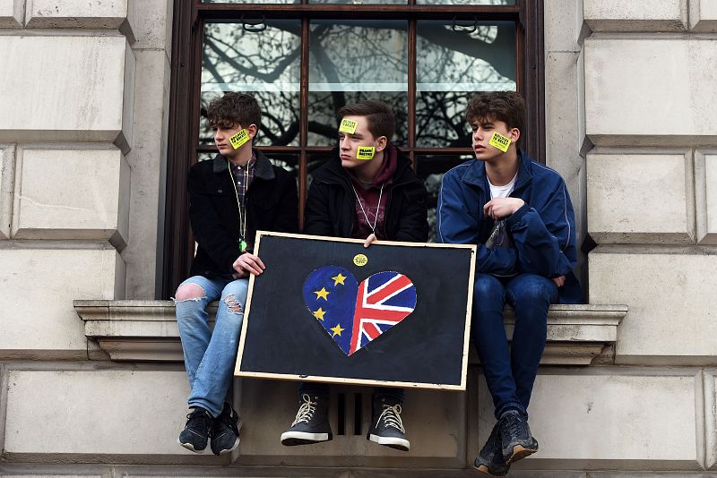 Tres jóvenes sostienen un cartel en el que se observa un corazón pintado con los colores de las banderas de la UE y del Reino Unido