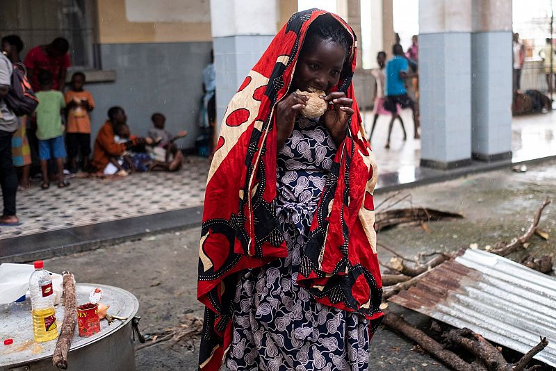 Una mujer se protege de la lluvia con un pañuelo mientras come un pedazo de pan en un campamento de refugiados improvisado en un instituto de Beira, Mozambique