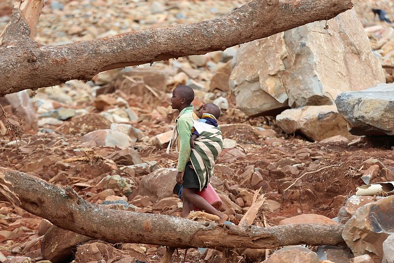 Un niño con un bebé en su espalda camina a través de escombros después del ciclón Idai en Ngangu, Chimanimani, Zimbabue