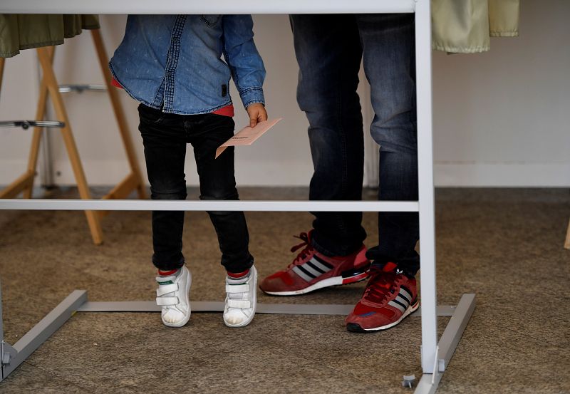 Un padre con su hijo en una cabina de votación en un colegio electoral de Pola de Siero, Asturias