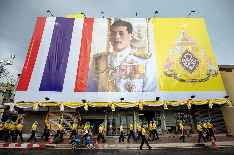 Varios voluntarios pasan bajo un cartel gigante del rey Vajiralongkorn antes del inicio de la ceremonia de coronación del monarca.