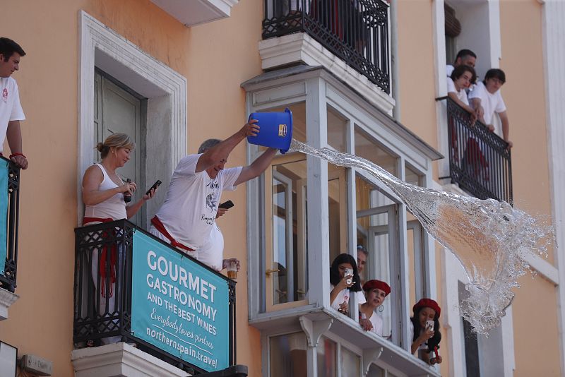 Un hombre lanza un cubo de agua a la gente antes del tradicional chupinazo en la plaza del Ayuntamiento de Pamplona