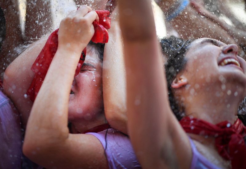 Varias personas abren sus brazos para recibir agua desde un balcón tras el lanzamiento del tradicional chupinazo