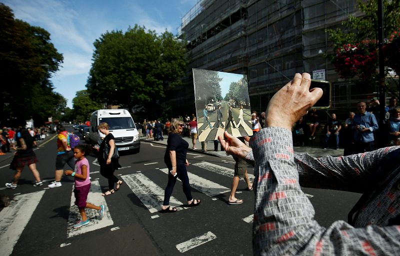 Una persona toma una fotografía del mítico paso de cebra mientras sostiene la portada de Abbey Road.