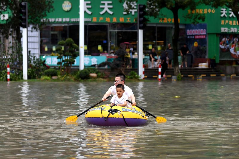 Un hombre y su hijo navegan en una lancha inflable durante las lluvias en China.
