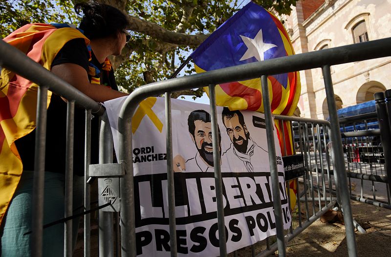 Detrás de una valla, se observa un cartel con la imagen de dos de los líderes independetistas presos, Jordi Sànchez y Jordi Cuixart, en el que se pide su liberación.