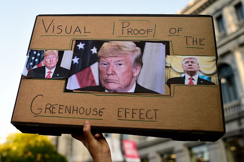 Un manifestante alza una pancarta en la que se ven varias fotografías del presidente de EE.UU., Donald Trump, con un texto que reza: "Prueba visual del efecto invernadero"