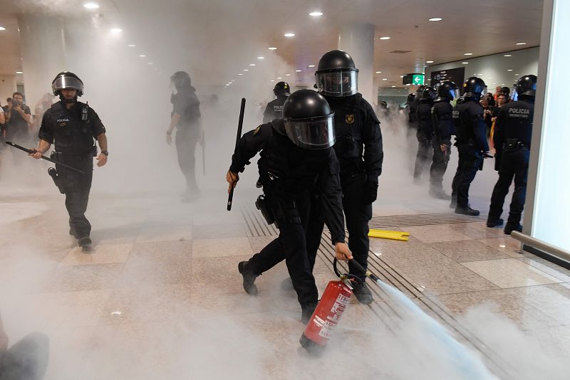 Un policía agarra un extintor de incendios dentro del aeropuerto rodeado por los manifestantes.