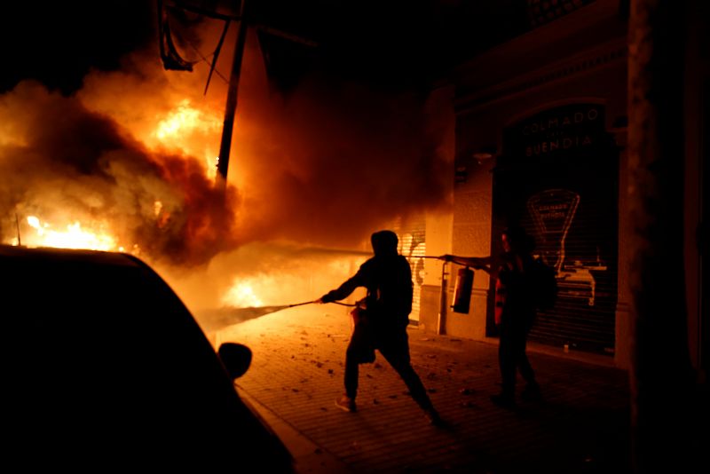Una persona intenta apagar las llamas de un automovil durante el tercer día de protestas en Barcelona.