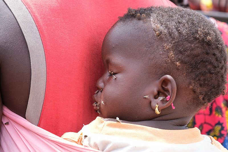 Una madre portando a su hija, acosada por las moscas negras, transmisoras de enfermedades. En Faladie, un campamento de desplazados de Mali