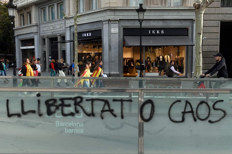 Manifestantes independentistas catalanes caminan junto a una pintada en la que se puede leer: "Libertad o caos".