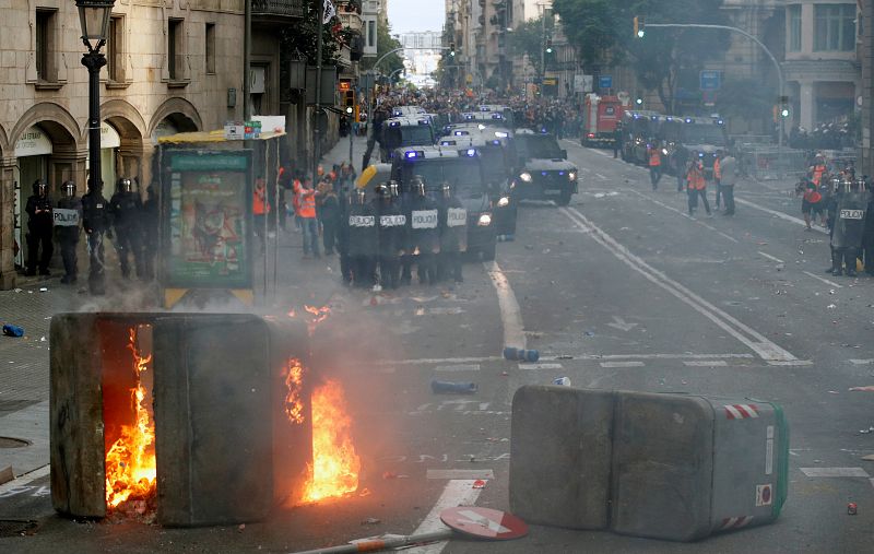 Antidisturbios vigilan la calle mientras arde un contenedor en el centro de Barcelona.