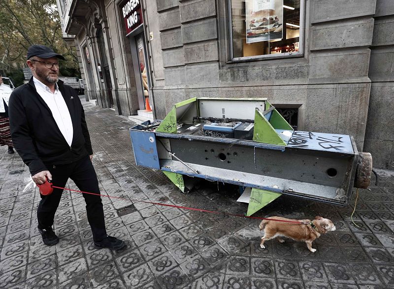 Un hombre pasea a su perro junto a una cabina arrancada este sábado en Barcelona tras los incidentes registrados anoche.