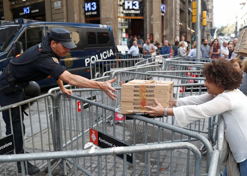 Una mujer entrega cajas de pizza a un agente a las puertas de la Jefatura de Policía en Barcelona. 