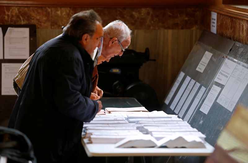 Dos hombres escogen la papeleta para después votar en un colegio electoral en Barcelona.