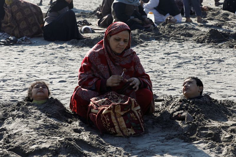 Una mujer se sienta cerca de sus hijos, enterrados hasta el cuello en la arena durante el eclipse solar, en la playa de Clifton, en Karachi. Muchos paquistaníes creen que enterrar a las personas con discapacidad en la arena durante un eclipse solar l