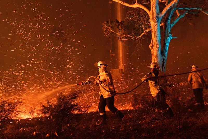 Los bomberos humedecen las brasas para proteger las casas cercanas