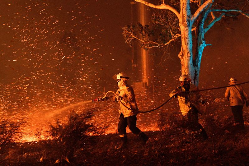 Los bomberos humedecen las brasas para proteger las casas cercanas