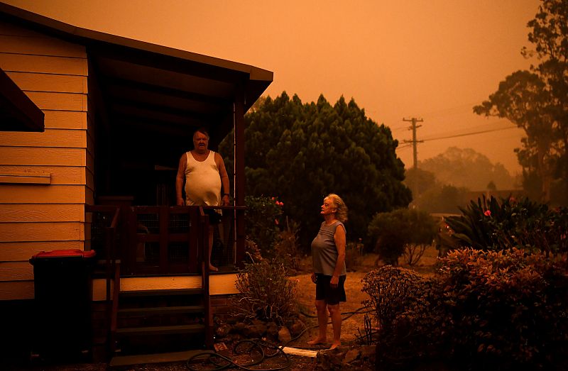 Nancy Allen y Brian Allen humedecen con mangueras su casa debido a que el fuerte viento empuja humo y cenizas procedentes del incendio de Currowan hacia Nowra