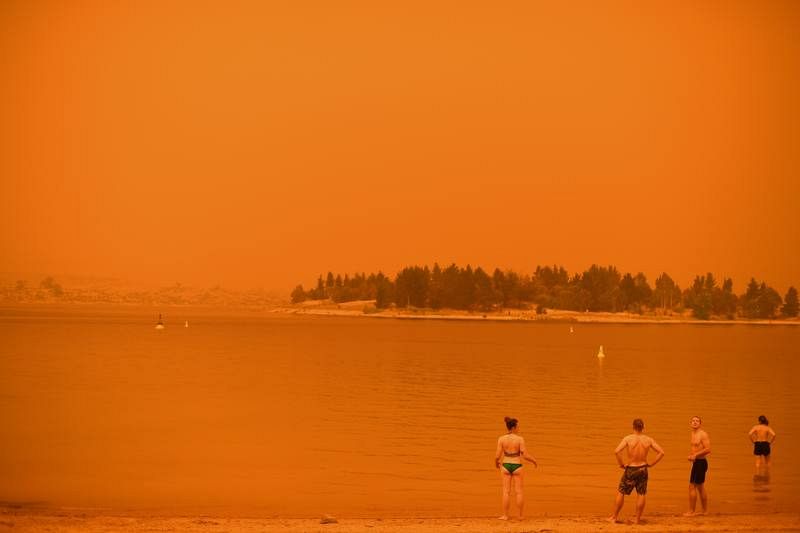 Un grupo de personas se refresca en el lago Jindabyne, bajo un cielo anaranjado debido al humo procedente de los incendios