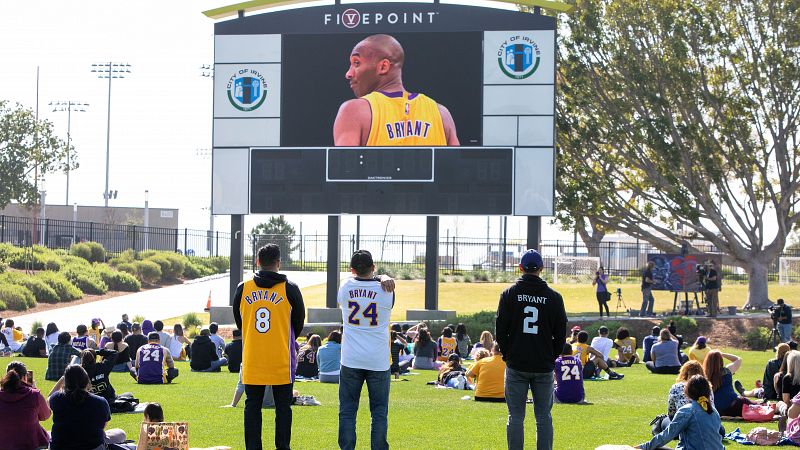 Varios fans observan la retransmisión del memorial de Kobe Bryant, su hija y los otros siete fallecidos, desde el Orange County Great Park soccer stadium en Irvine, California