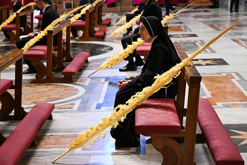 Una monja sentada junto a unas ramas de palma en una basíla de San Pedro vacía durante la celebración del Domingo de Ramos en el Vaticano.