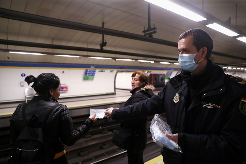 Un agente entrega mascaras faciales en una estación de metro de Madrid.