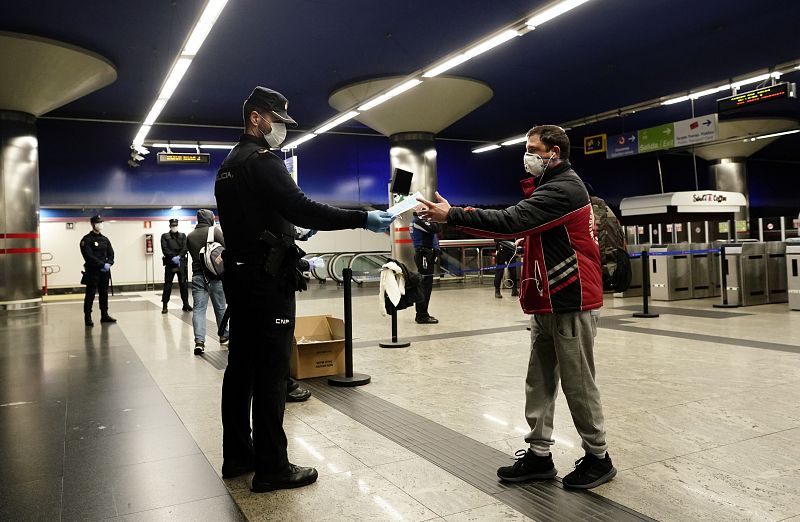 Un policía entrega mascarillas gratuitas a los pasajeros del metro de Madrid.