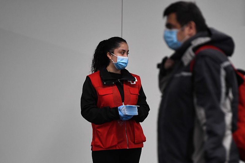 Una voluntaria de la Cruz Roja reparte mascarillas a los viajeros en la estación de Chamartín de Madrid.