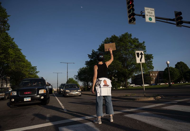 Un manifestante sostiene un cartel en un cruce peatonal mientras el resto marchan desde la Mansión del Gobernador al edificio del Capitolio del Estado de Minnesota.