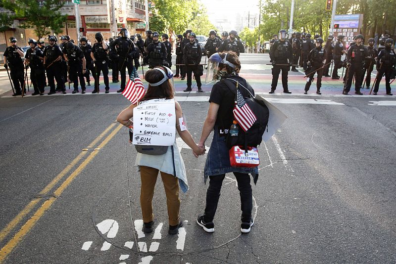 Una pareja se coge de la mano mientras la policía de Seattle vigila una manifestación contra la muerte de George Floyd.