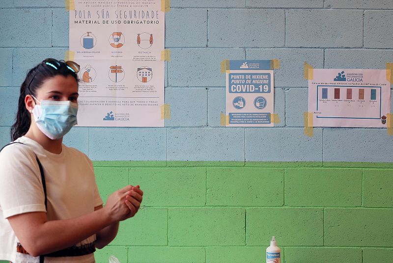 Una mujer se dispone a votar mientras pasa frente a numerosos carteles con las medidas preventivas para el COVID-19, este domingo en el pabellón dos Castros de Burela (Lugo).