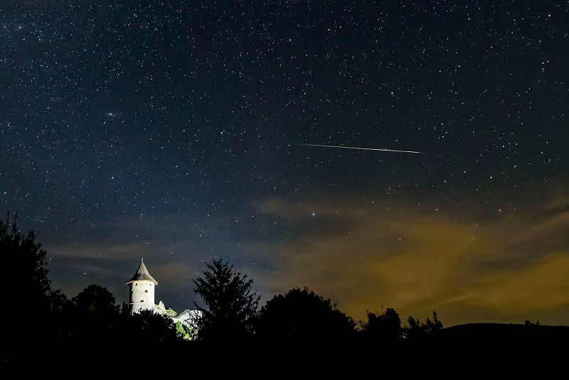 Una estrella fugaz cruza el cielo sobre el castillo de Somosko visto desde Salgotarjan, Hungría.