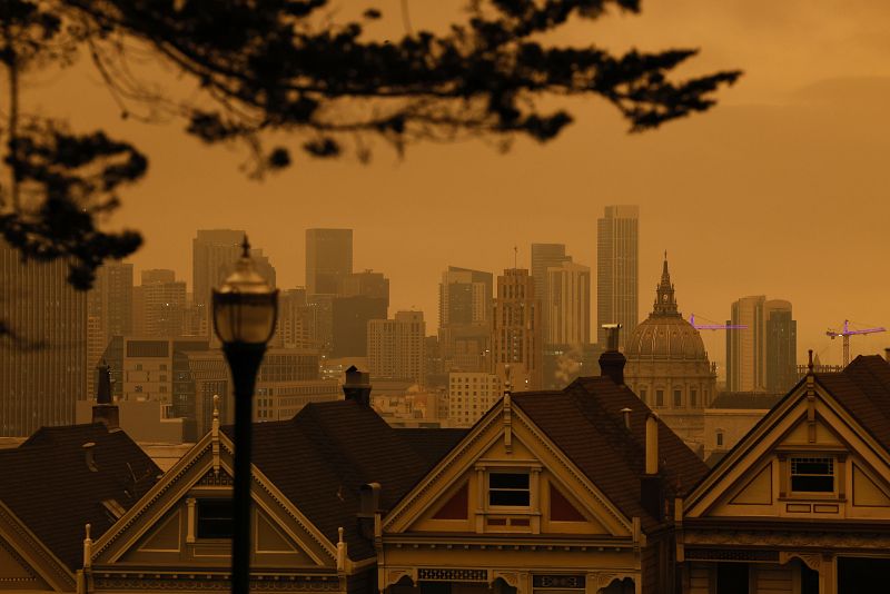 Una vista de Painted Ladies, la icónica hilera de casas victorianas históricas con un telón de fondo en el centro, bajo un cielo nublado naranja por la tarde en San Francisco, California, (EE.UU.).