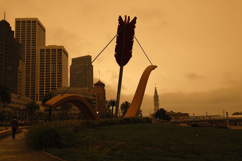 Vista de Cupid's Span, una escultura de Claes Oldenburge y Coosje van Bruggen y la Torre del Reloj del Ferry Building al fondo bajo un cielo nublado naranja en San Francisco.