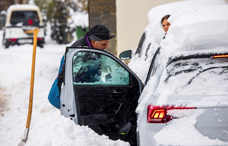 un hombre despeja la nieve para poder acceder a su vehículo en el pueblo de Pajares (Asturias).