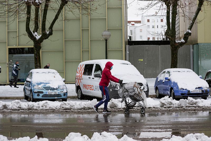 Una mujer camina por la calzada empujando un cochecito de bebé al lado de una acera prácticamente intransitable a causa la nieve en Vitoria.