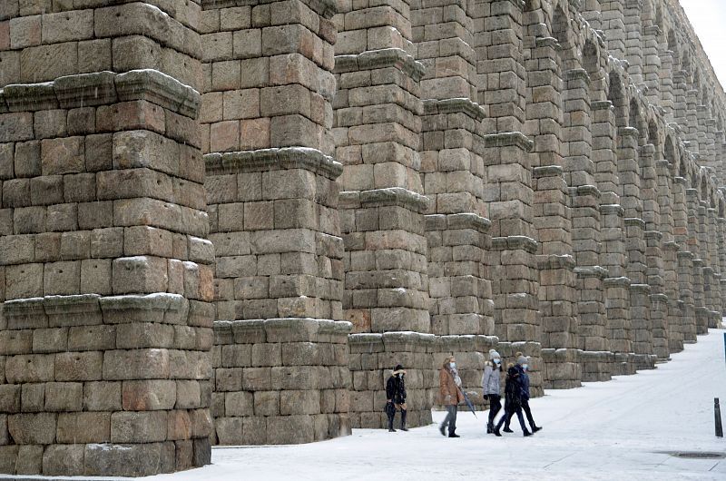 Varias personas pasan por debajo de los arcos del Acueducto de Segovia durante una intensa nevada.