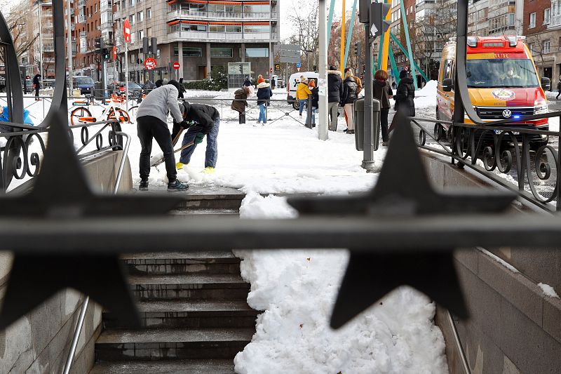 Varias personas limpian la nieve en el acceso a una estación de metro en Madrid.