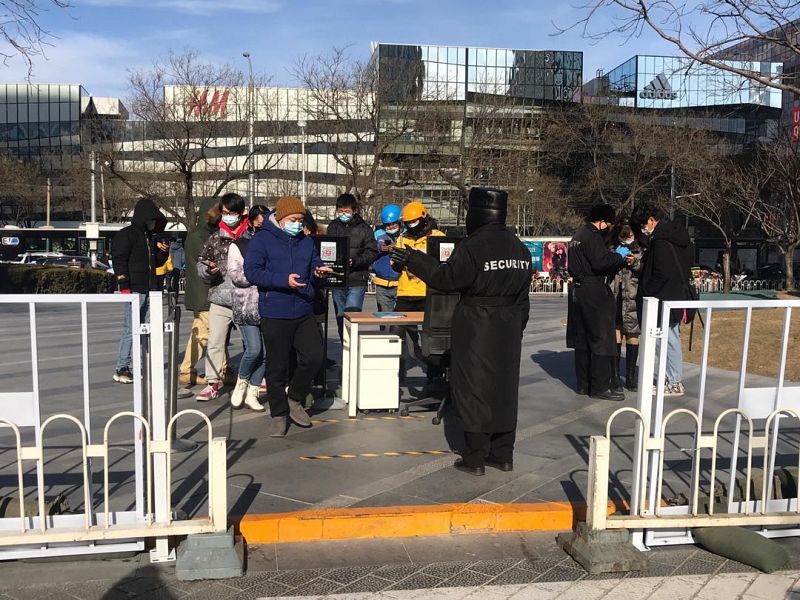 Varias personas esperan para que un vigilante compruebe su estado de salud a través de una aplicación móvil en Pekín