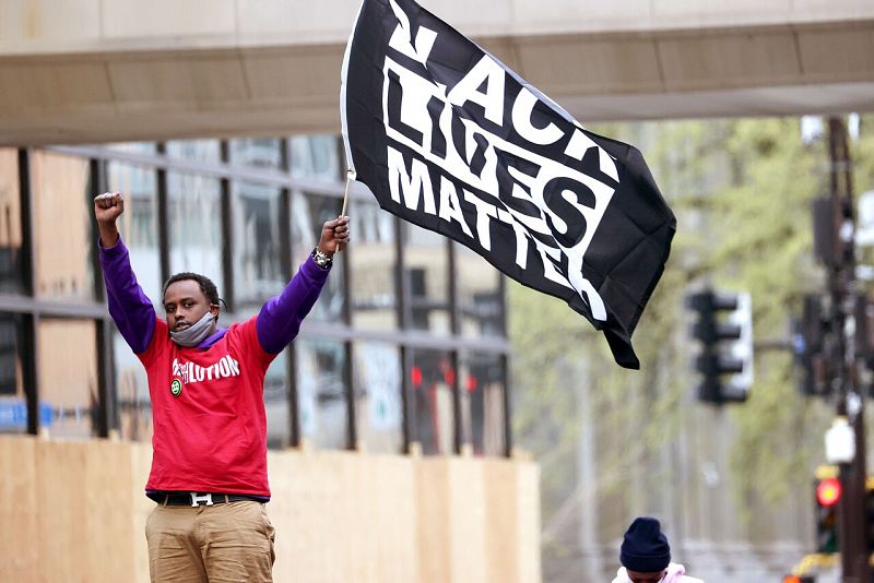 Un hombre levanta los brazos en señal de victoria mientras posa con una bandera con el lema Black Lives Matter