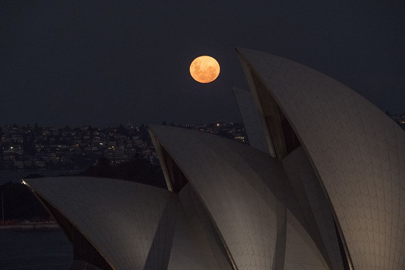 La luna llena se eleva detrás de las velas de la ópera de Sydney, Australia.