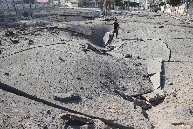 Un joven palestino toma fotografías con su smarthone de un enorme cráter en una carretera principal en la ciudad de Gaza.