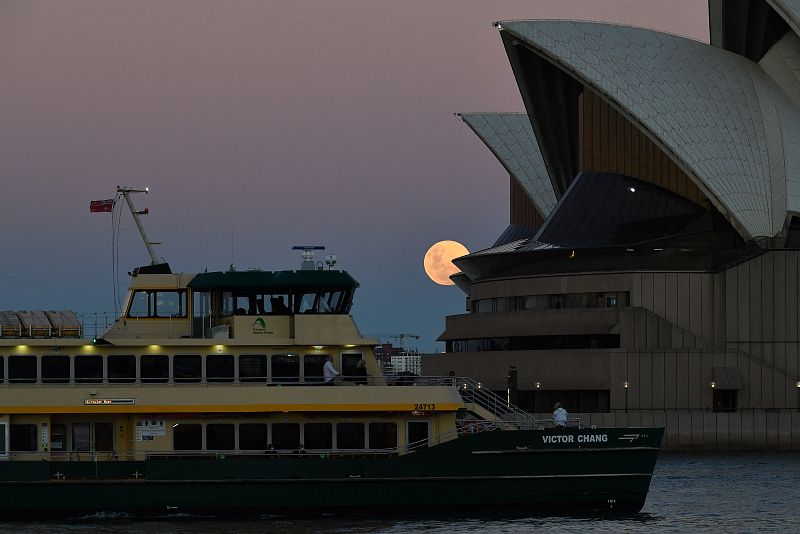 Un ferry pasa mientras la Luna, detrás, se eleva sobre la Ópera de Sydney.