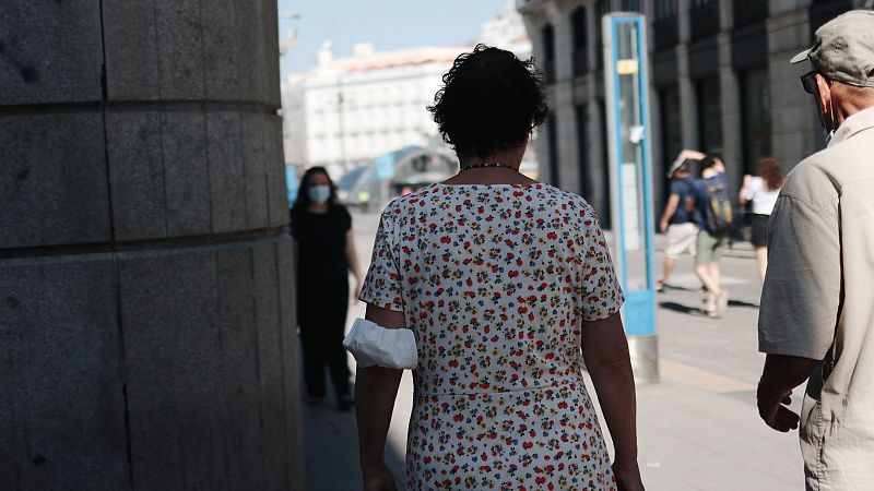 Una mujer pasea por el centro de Madrid con la mascarilla a mano.