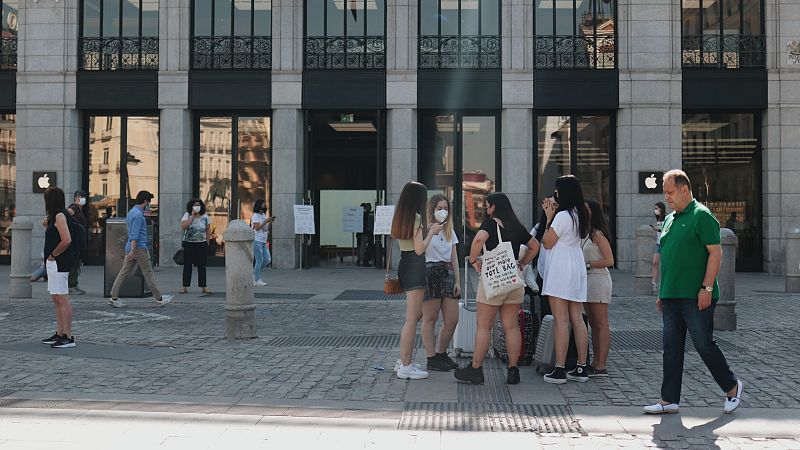 Un grupo de jóvenes charla en la calle con mascarilla, mientras un hombre camina sin ella en la Puerta del Sol, Madrid