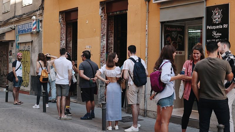 Personas con y sin mascarilla hacen cola en la calle para entrar en una cafetería